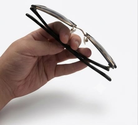 Hand holding a pair of eyeglasses against a white background