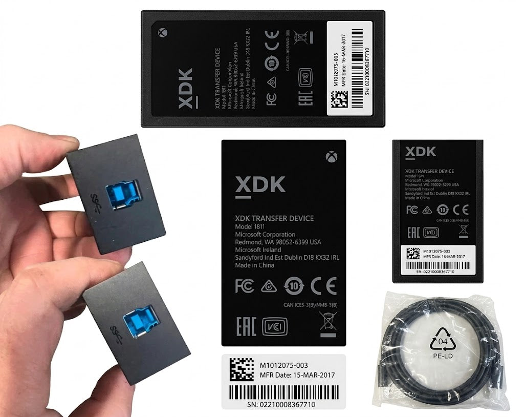 XDK transfer device battery pack set with a hand holding two small dark gray rectangular batteries with blue USB-C connectors, alongside larger battery packs, a cable, and printed product labels on a white background.