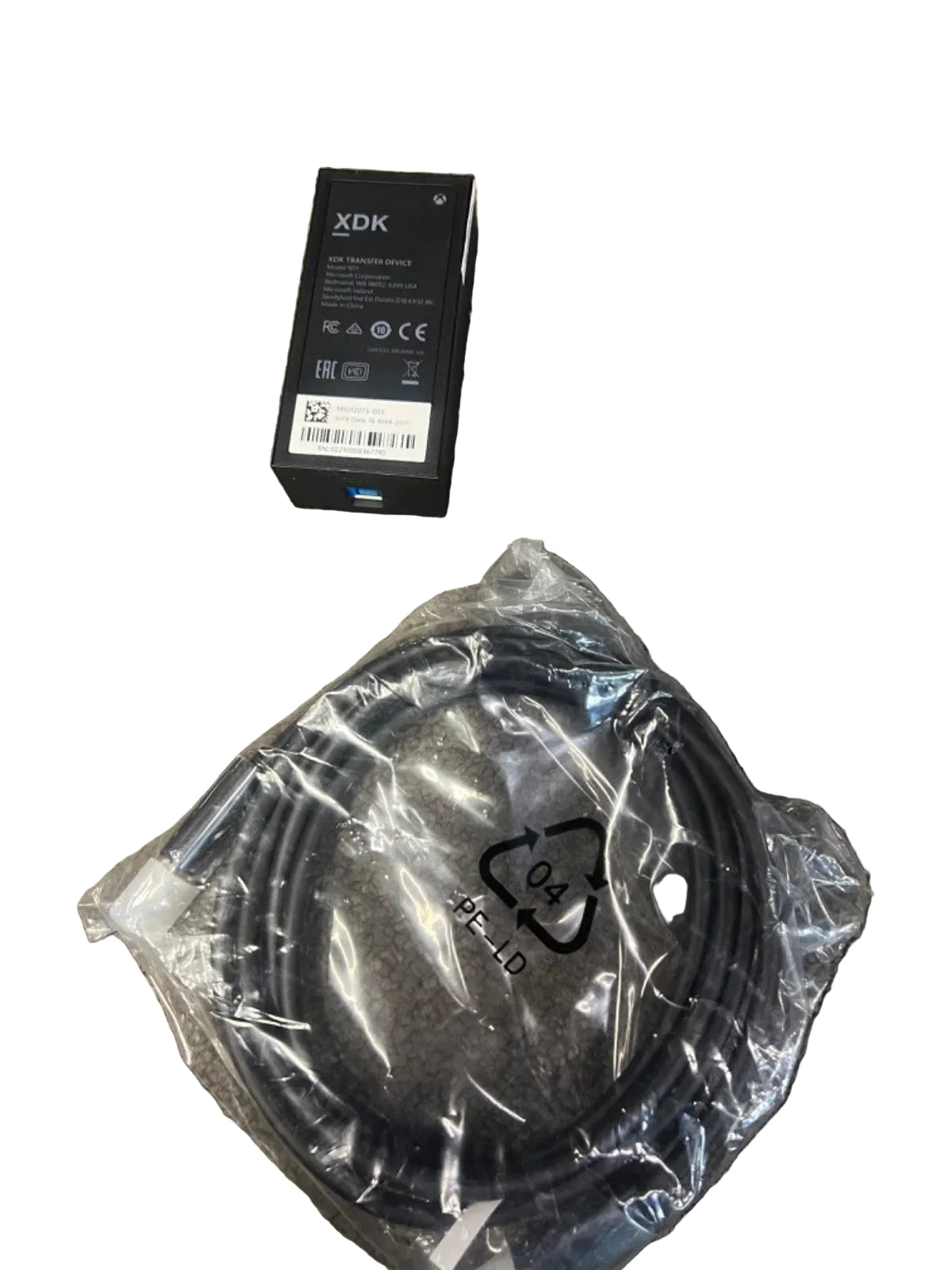 A black XDK electronic component in its original box next to a coiled black cable sealed in a clear plastic bag, placed on a textured gray carpet.