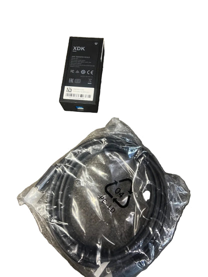 A black XDK electronic component in its original box next to a coiled black cable sealed in a clear plastic bag, placed on a textured gray carpet.